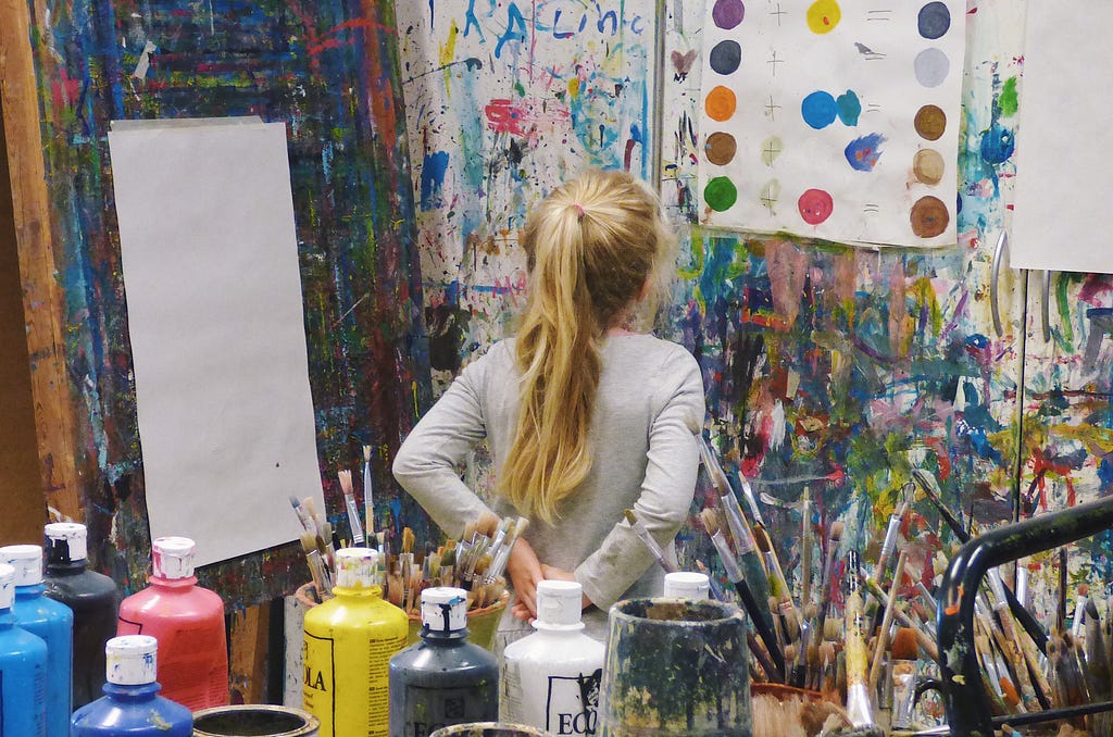 a girl looking at wall full of paints and canvas