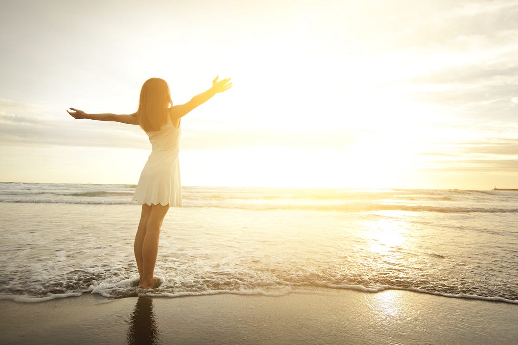 A woman with her arms up by the beach.