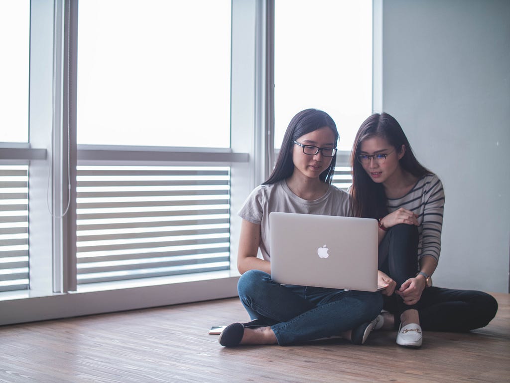 two students, women discuse in front of they laptop