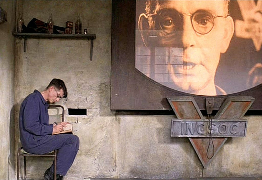 John Hurt as Winston Smith in the 1984 version of George Orwell’s novel 1984. He sits to the left of his ever-spying, one-way telescreen, writing in his secret diary.