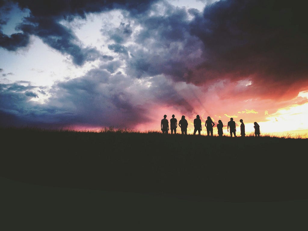 A group of people silhouetted in front of a setting sun