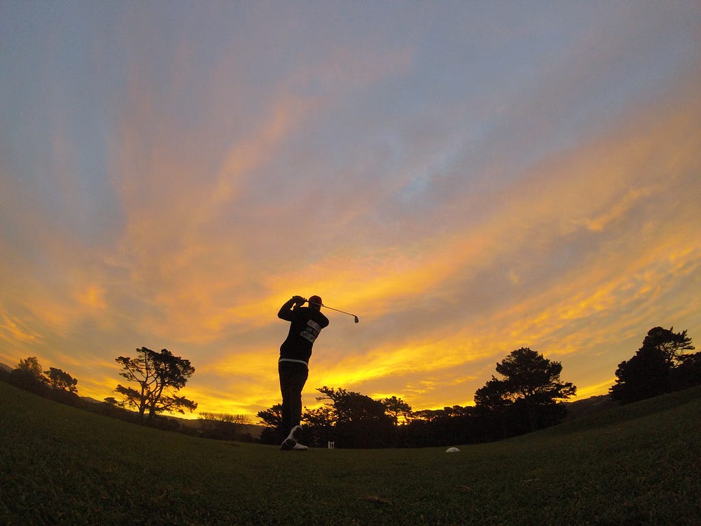 A person hitting a golf shot at sunset.