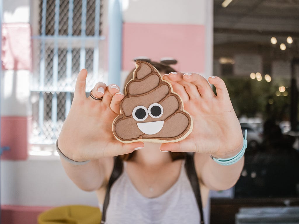A person holding up a cookie shaped like the poop emoji