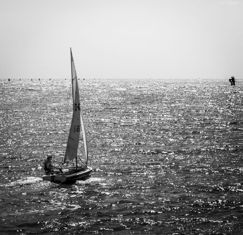 A small sailboat forges through small waves out to sea, charting a course for an uncertain future.