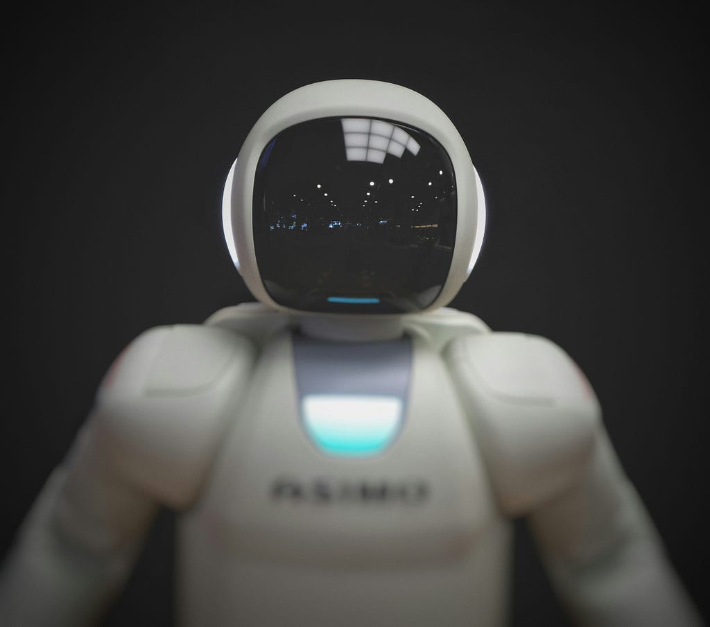A toy-like robot faces the camera. Its face is a black screen similar to a computer monitor.