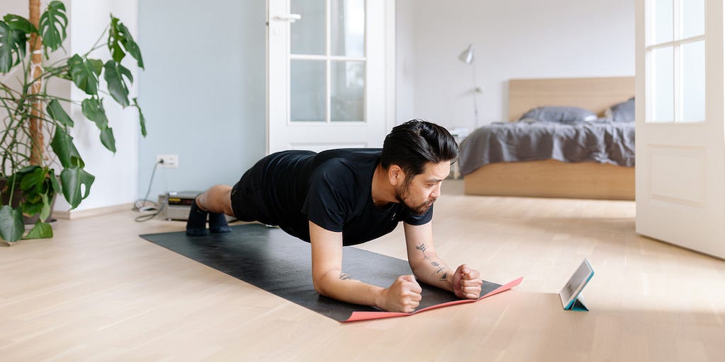 young man planking on yoga mat while watching smart tablet screen
