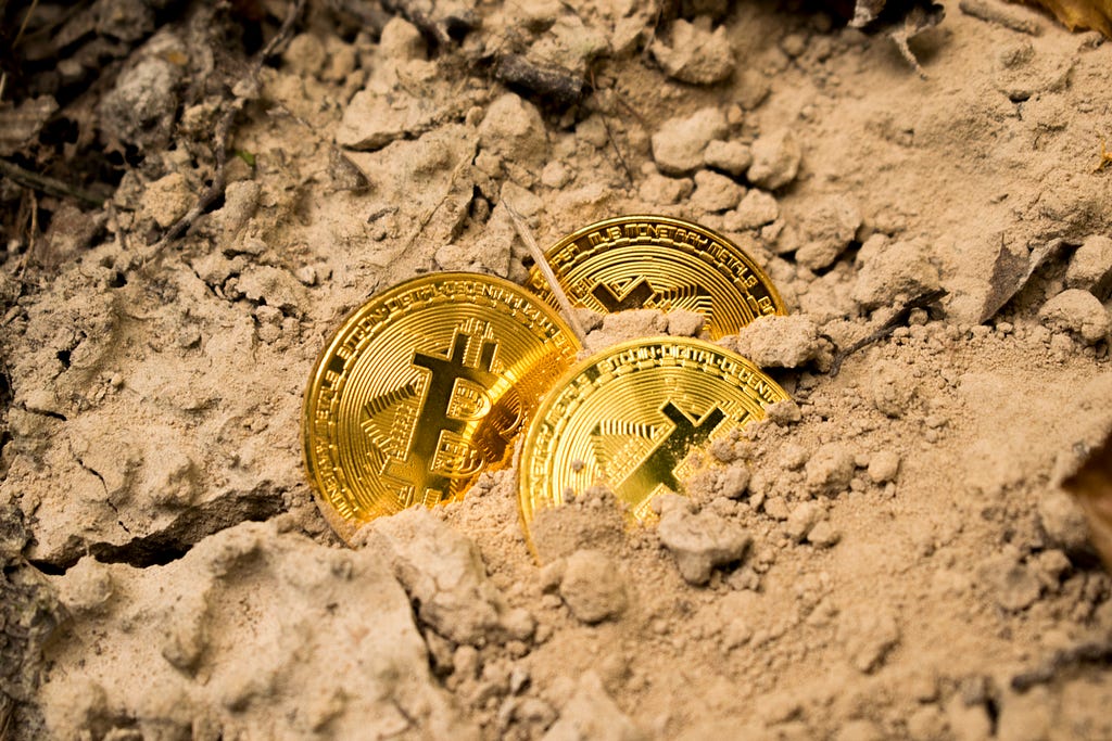 Three coins with the Bitcoin logo on them lying in some dirt