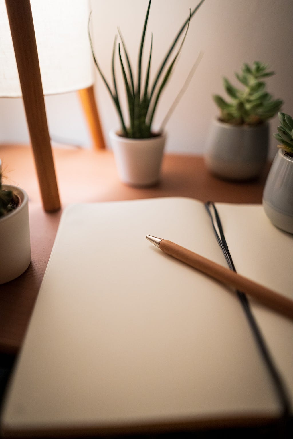 A notepad with a pencil resting on a table with a flower vase in front of it.