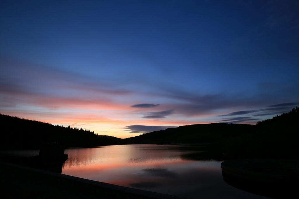 sunset with gentle hills rising on either side of a lake reflecting the fading light of the evening sky