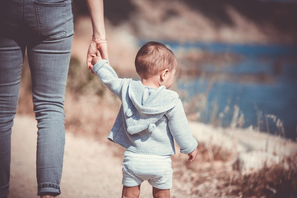 Mother holding her toddler’s hand by a lake