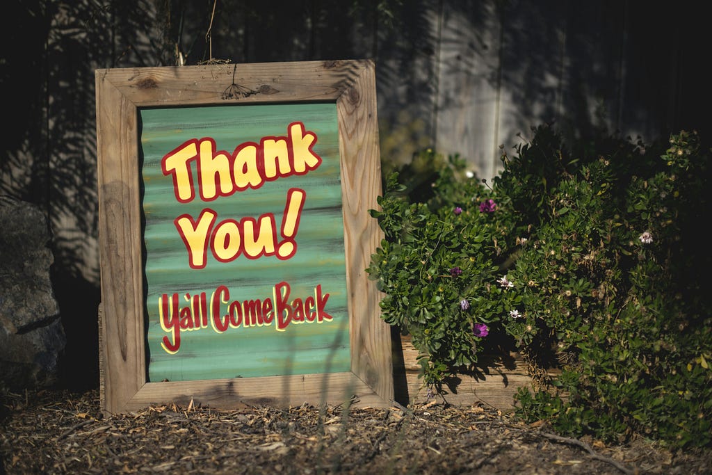 This image depicts a small sign with the words “Thank You! Y’all Come Back” written on it.