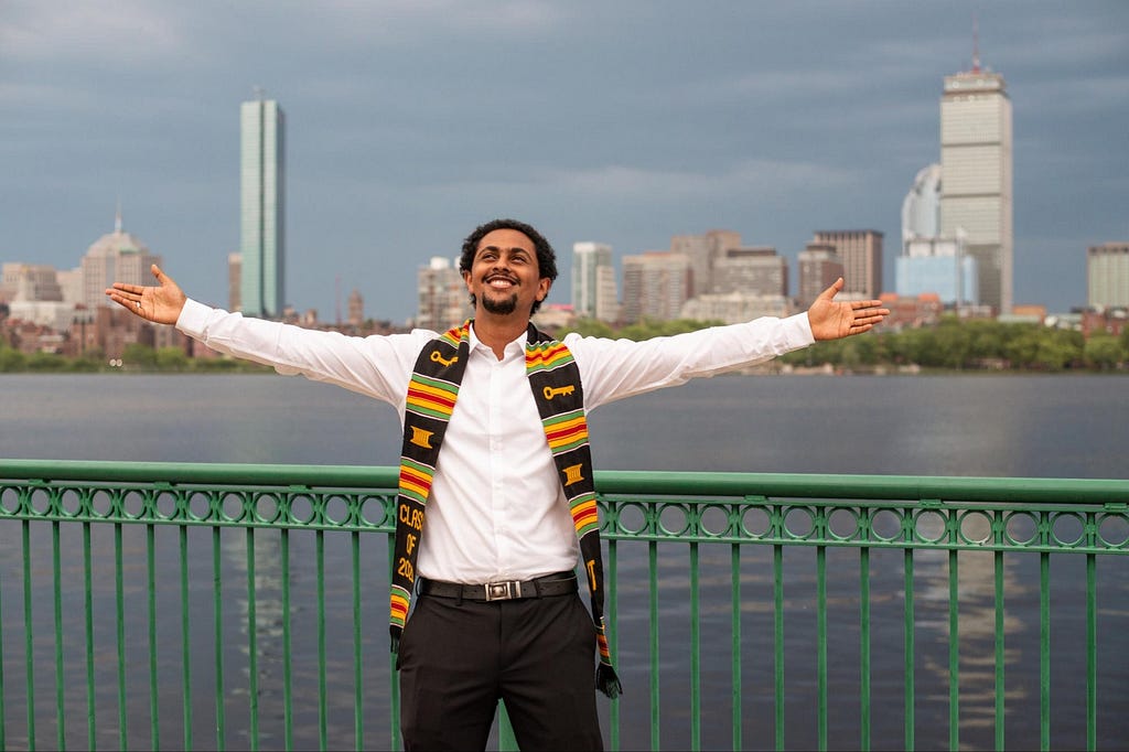 Man with arms outstretched in front of the Charles River.