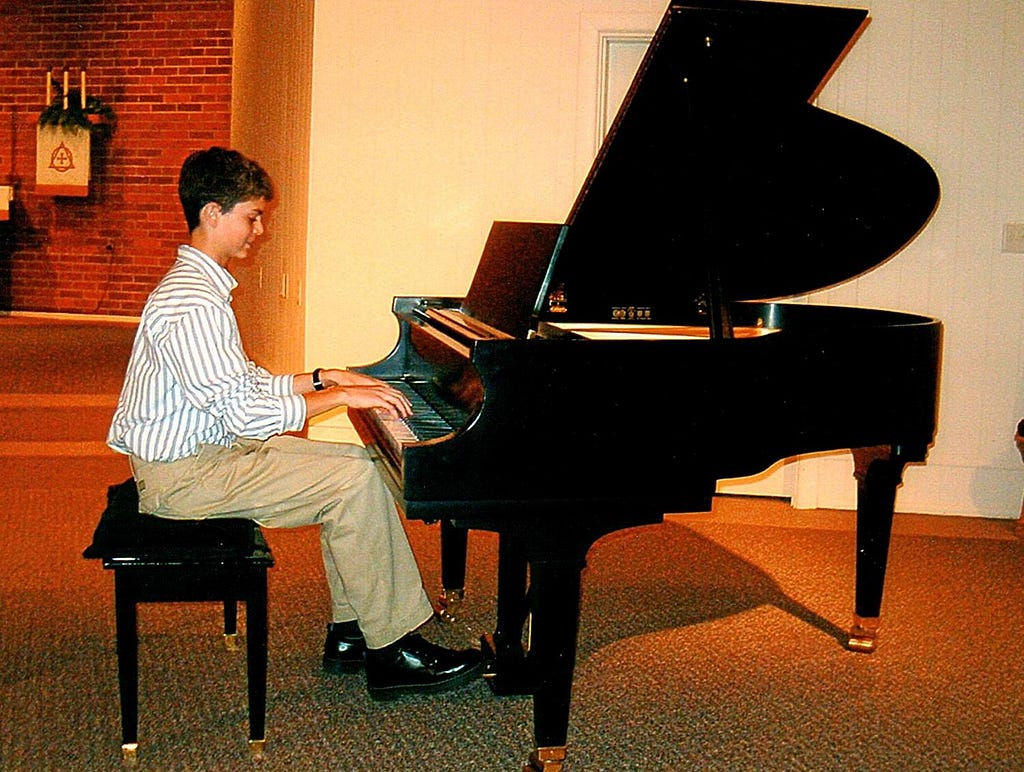 Luke Brenneman, in contrast to running photos is show in a dress shirt and slacks, seated and playing a grand piano.