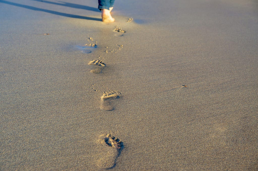 foot prints in the sand- you can see the feet of someone walking out of the image