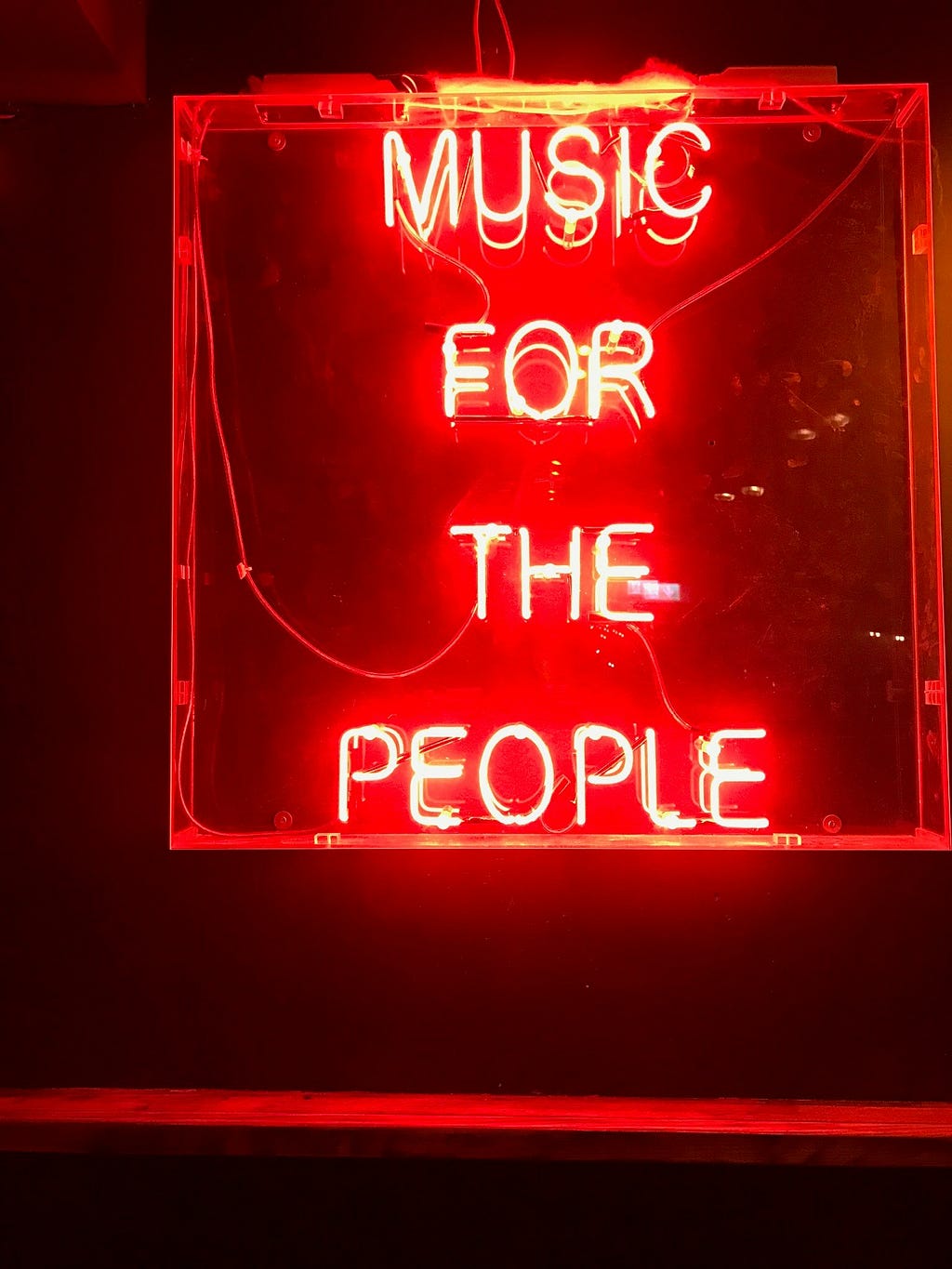 A picture of a sparkling red neon light that bears the words: ‘Music for the people’.