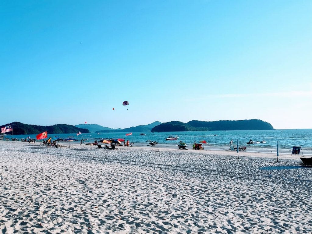 white sands  blue waters people on the beach at Pantai Cenang in Langkawi