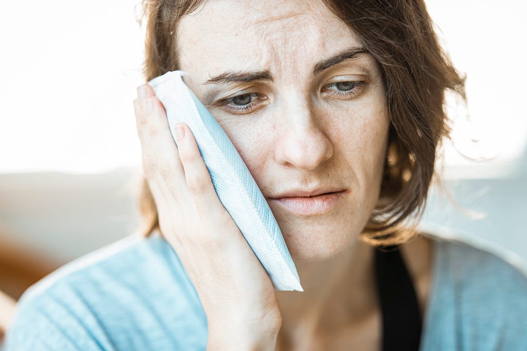 women in stress, pressing an ice pack on her cheek.