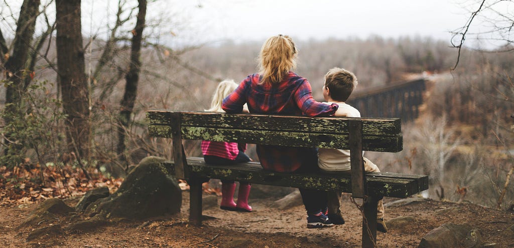 mom sits on a bench with 2 children contemplating nature