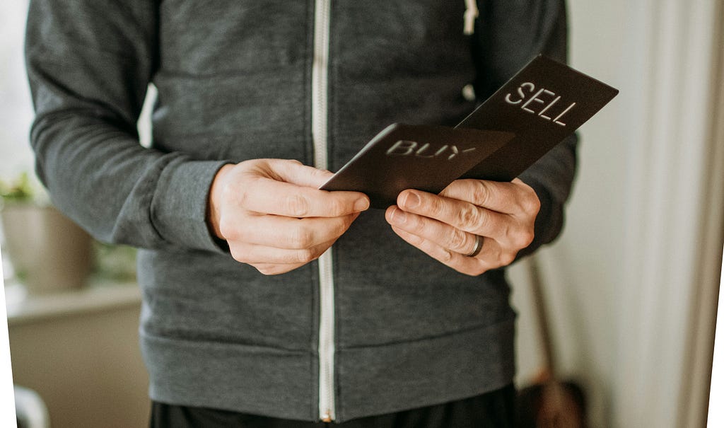 An image of a man holding a postcard that communicates whether to buy or sell crypto.