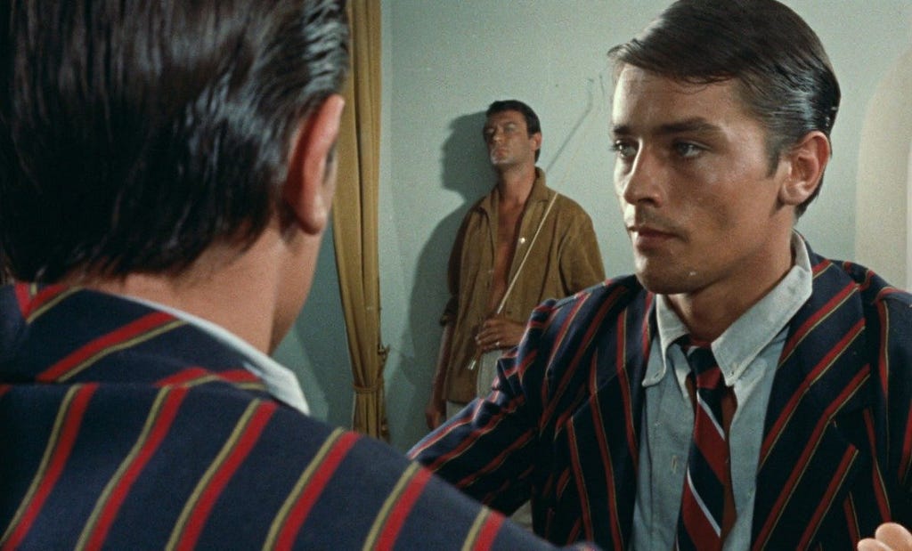 A man standing in front of a mirror in a pinstripe suit glances to see another man coldly staring at him from behind.