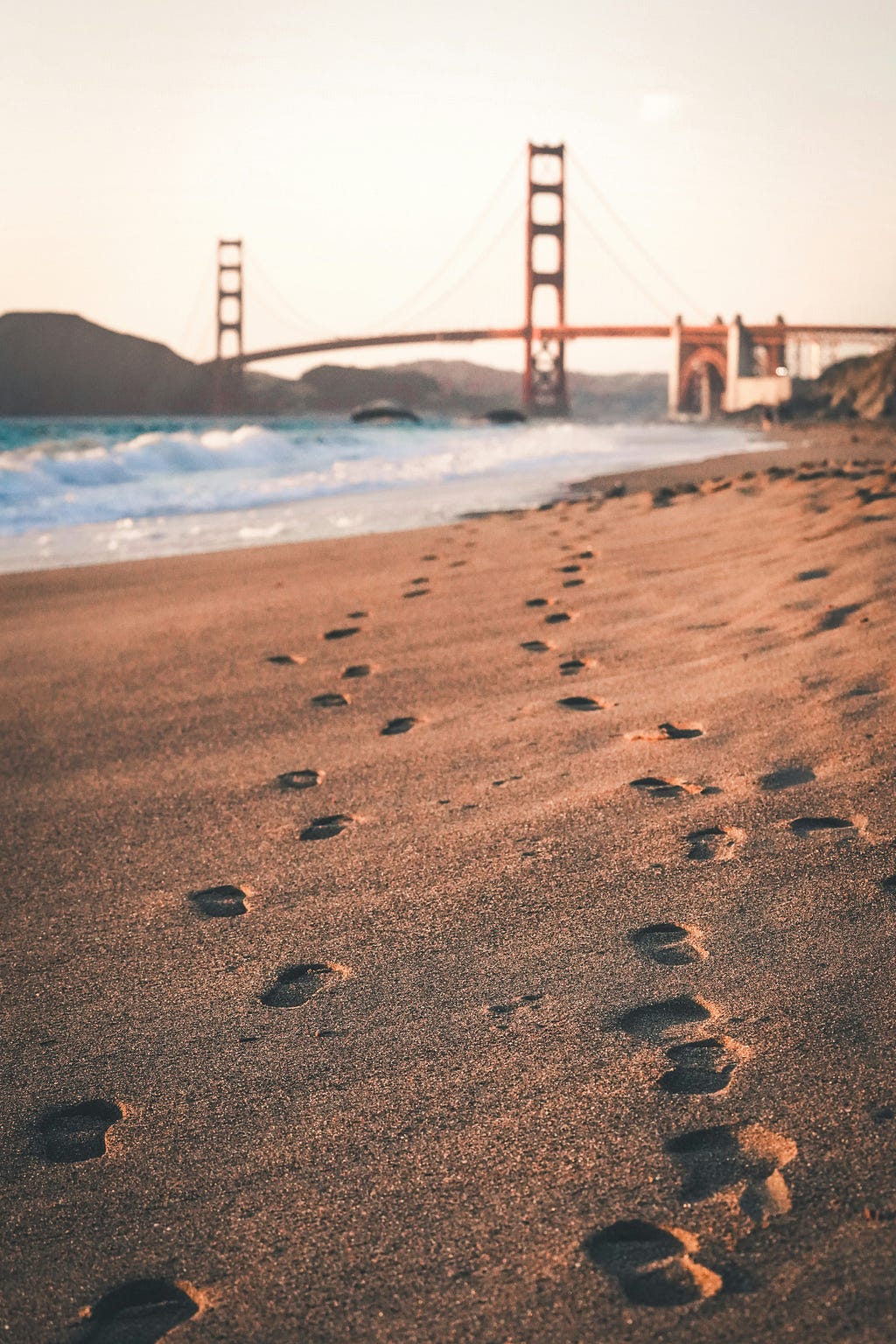 A picture of footprints in the sand with a waterbody and a bridge at the horizon, used to signify the journey and the hope that waits beyond.