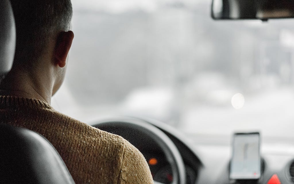 View from the backseat of a car, with a man driving and a phone mounted on the dashboard