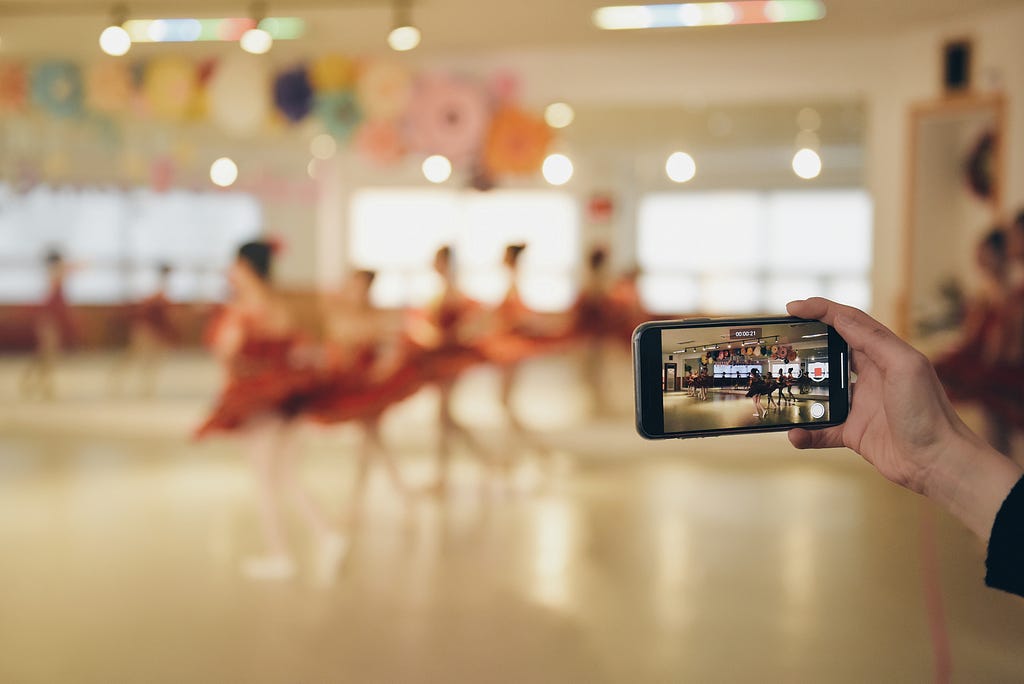 A smart phone is recording a video of several ballerinas in pink costumes.