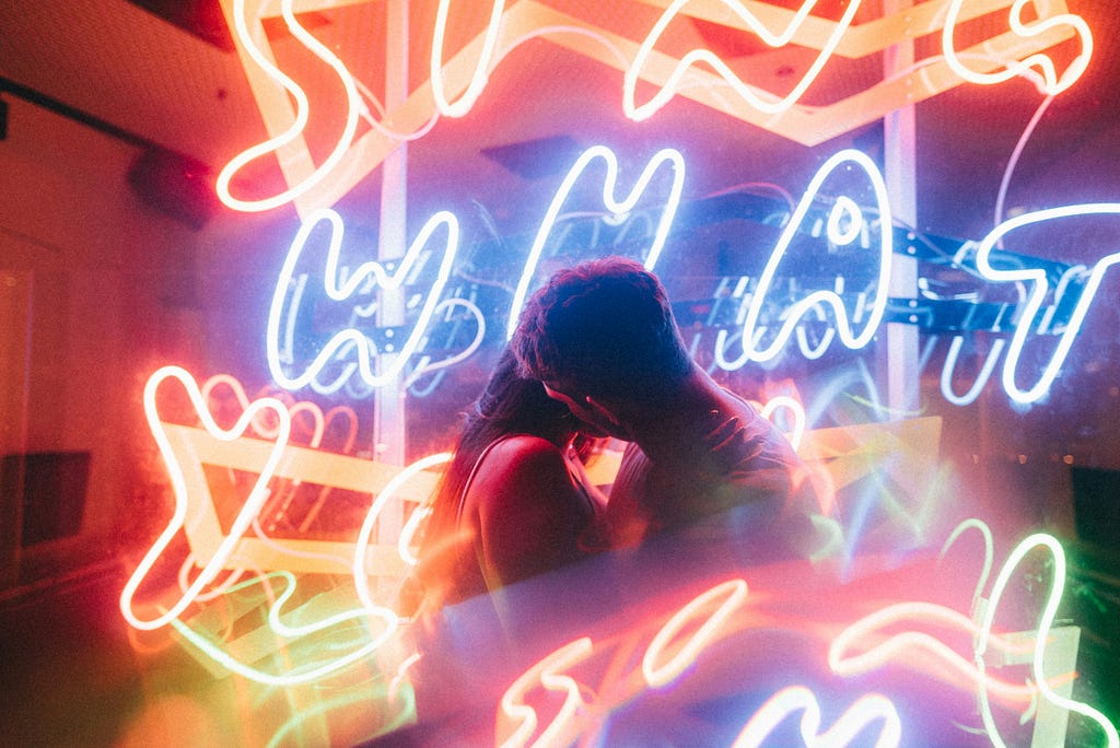 A couple kissing with neon signs around them