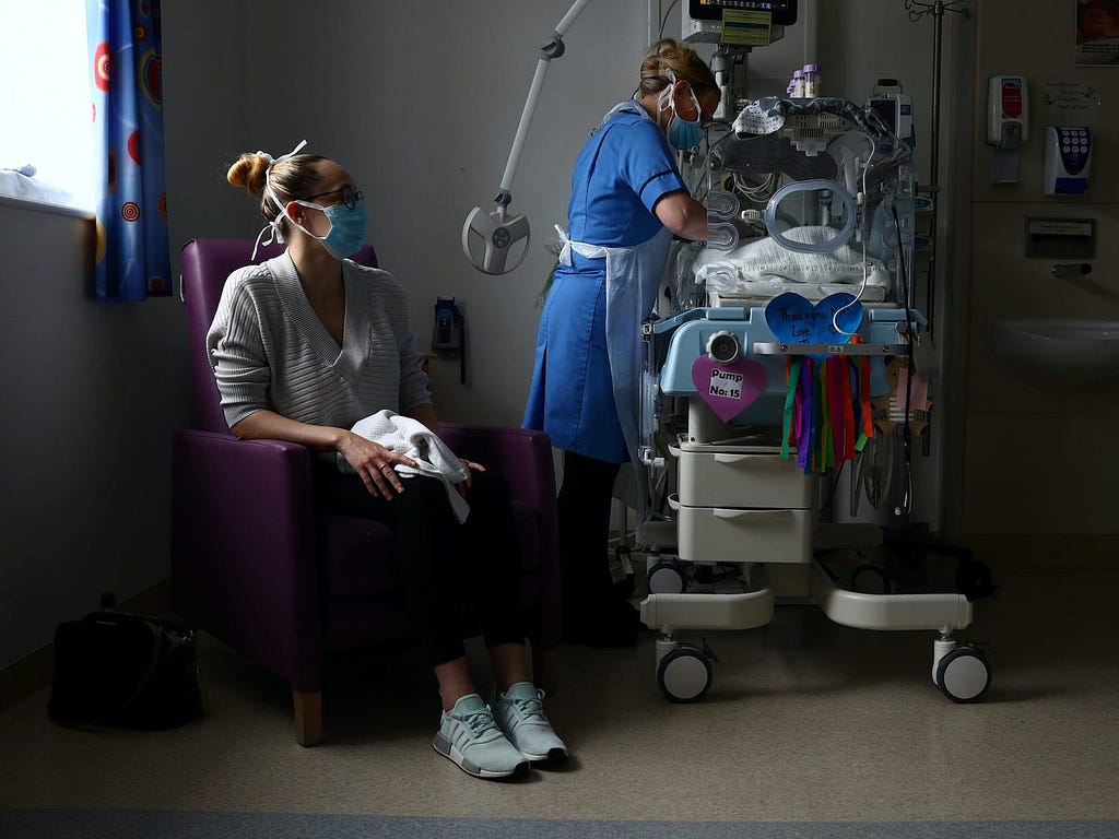 A nurse cares for a premature baby as his mother looks on amid the coronavirus pandemic.