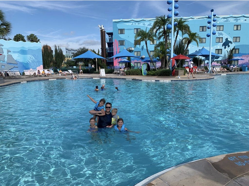 The author and his four children swimming in a relatively empty swimming pool at Disney’s Art of Animation Resort.