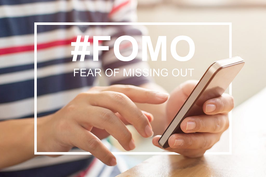 An image with '#FOMO, fear of missing out'. Close-up image of male hands using mobile smartphone.