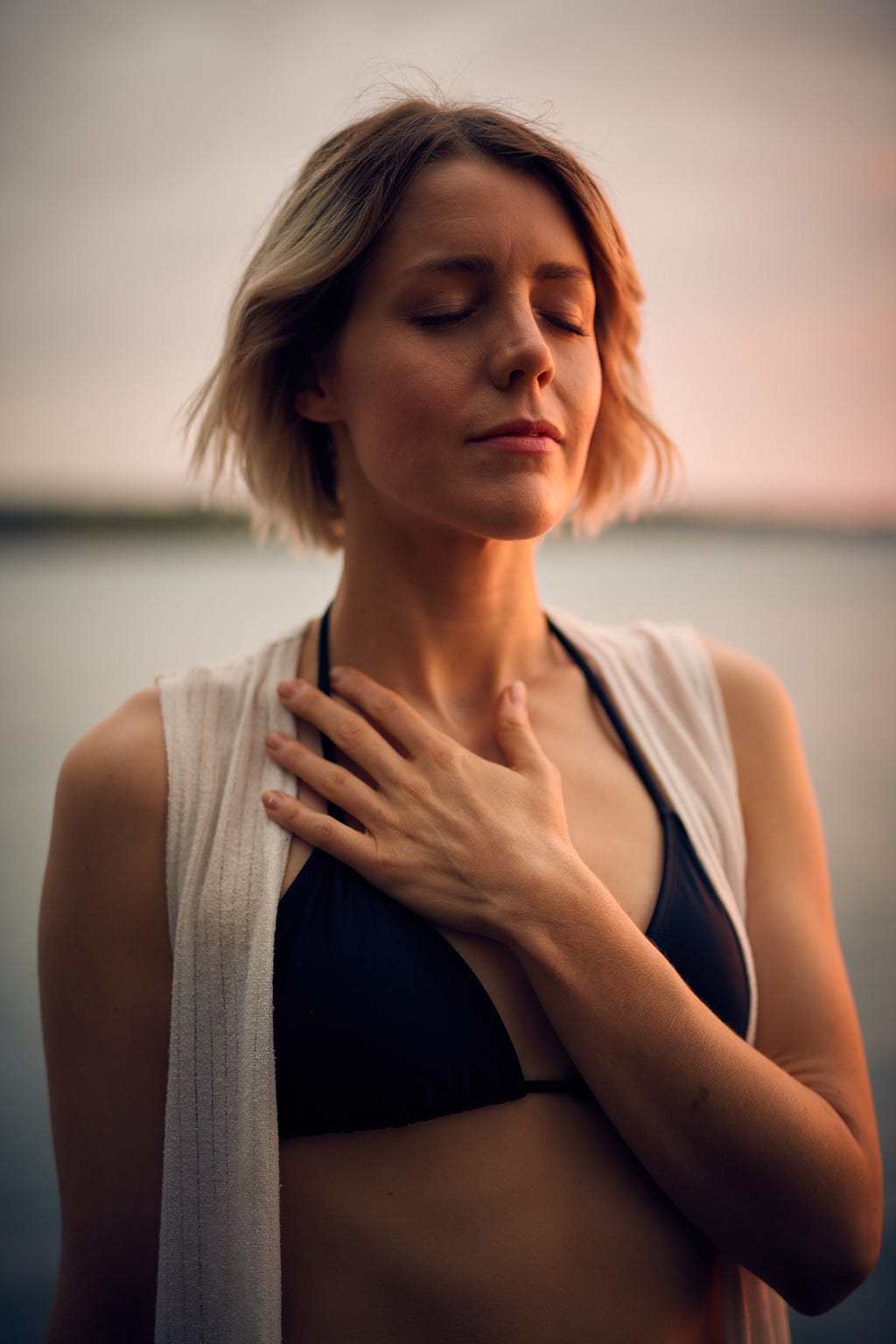 woman with medium blond hair holding her palm to her chest and looking calm.