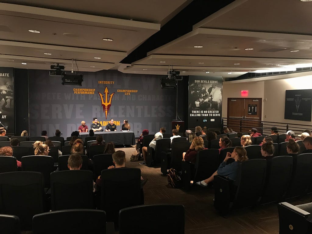 Student-athletes from Arizona State sit in an auditorium watching and listening to the innovation panel.