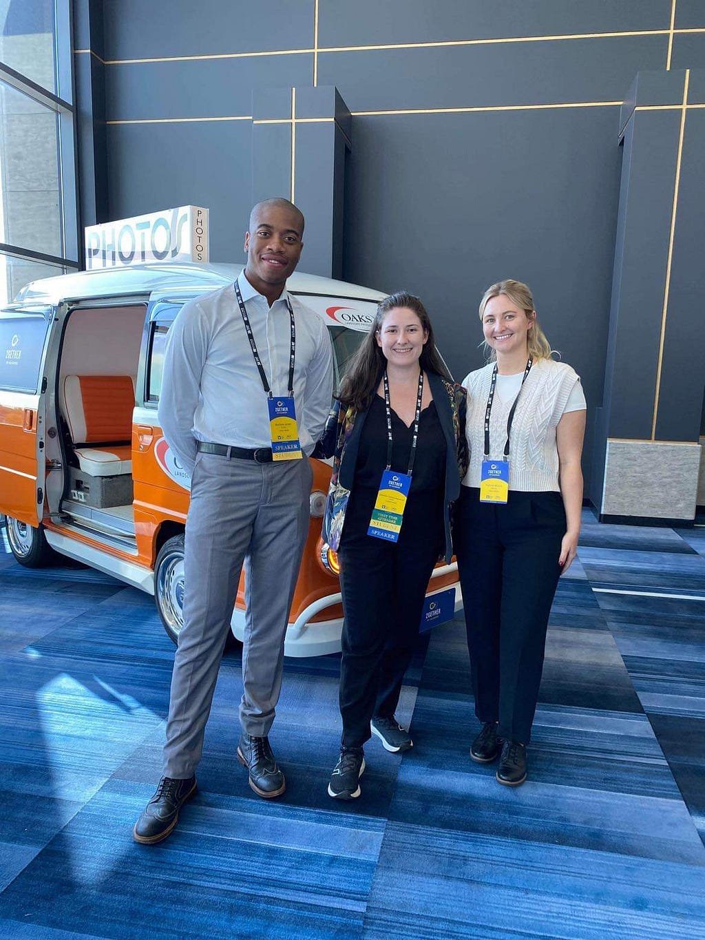 Matthew, Catherine, and Patti posing for a photo in front of an orange camper van prop.