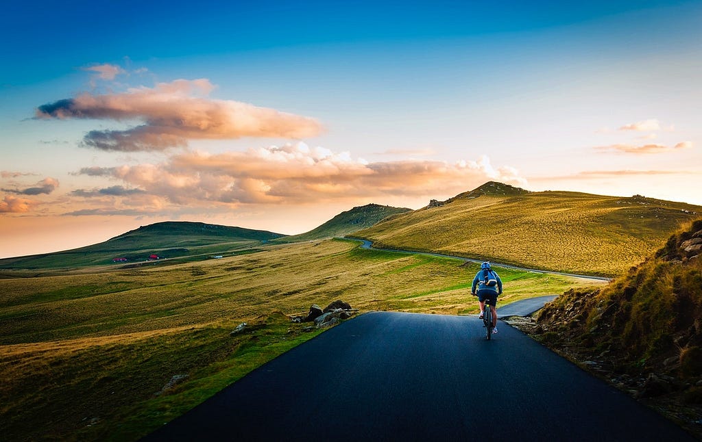 Man on a mountain road cycling towards the rising sun.