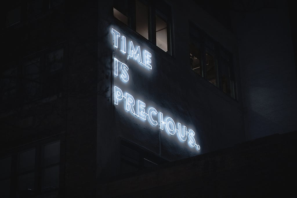 A white neon sign illuminated at night on a building saying “time is precious”