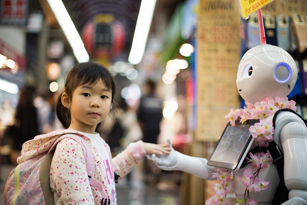 A little girl wearing a backpack holds the hand of a robot.