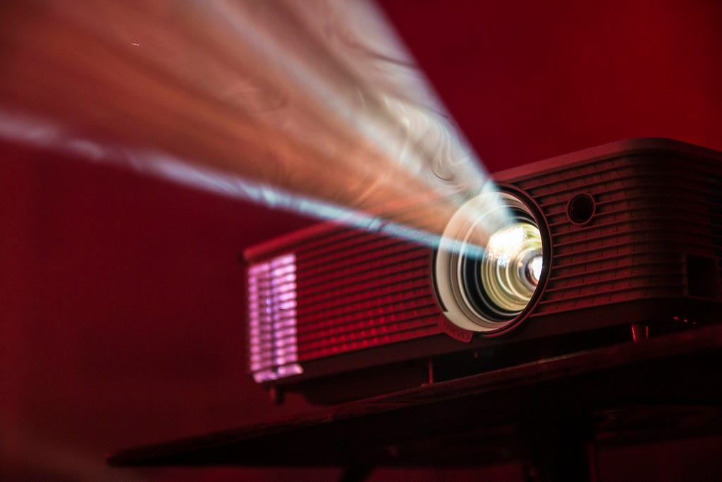 A projector lets out a bright, conical light in a dark room.