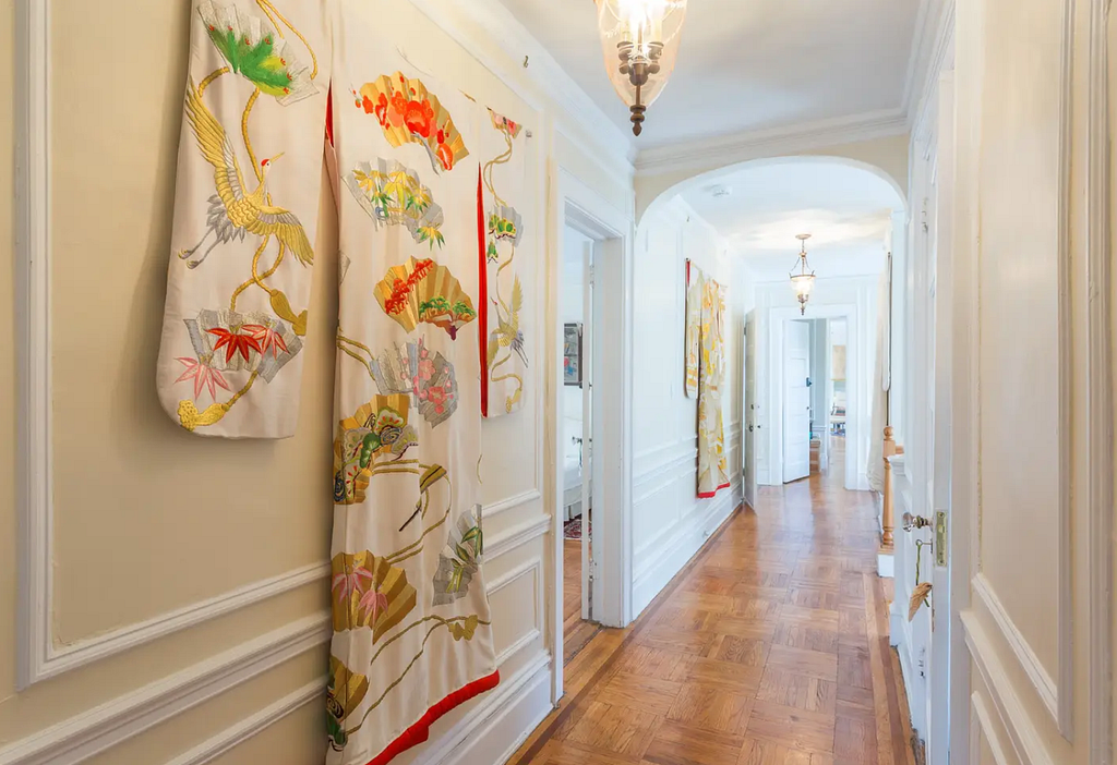 A sunlit hallway is decorated with brightly colored silk kimonos on the walls.