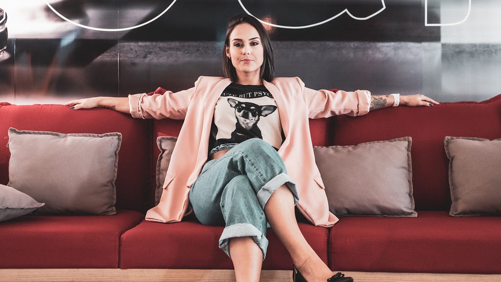 Woman sitting on a red couch arms wide open to the sides and legs crossed looking confident.