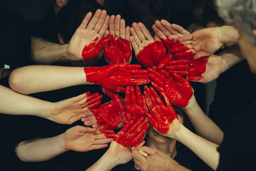 15 hands placed together with red paint on them resembling the shape of love.