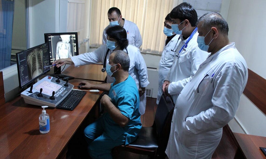 Six health care professionals stand around a screen that displays X-ray diagnostics of a patient being tested for TB.