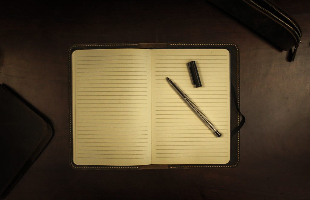 Open writing pad with no writing, pen with top off lying on pad