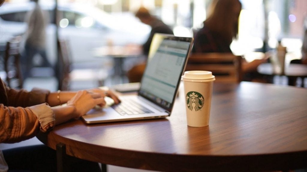 Solo customer, sitting at a round table at Starbucks with a laptop and coffee by their side.