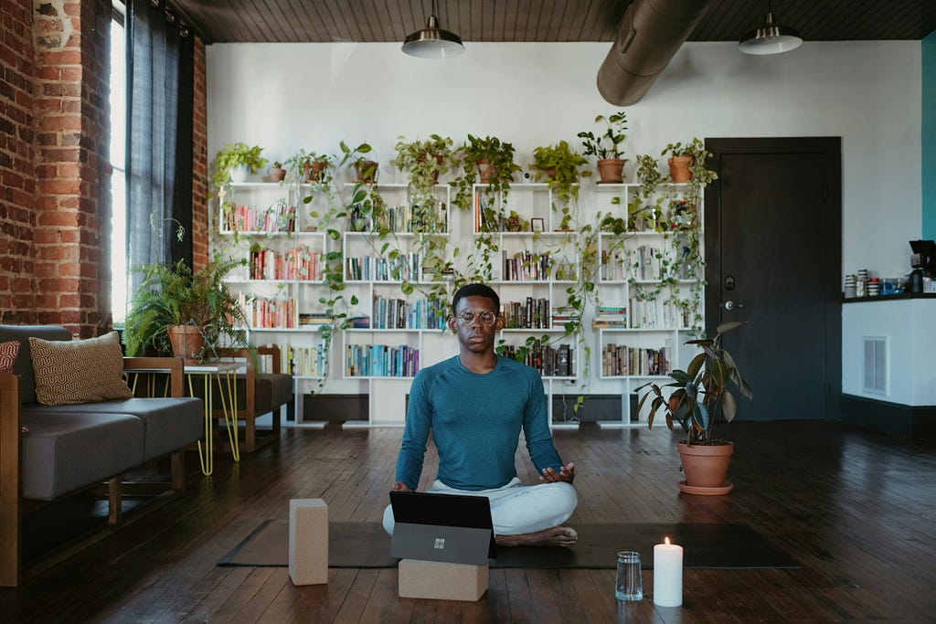 A man practicing meditation while using his laptop and tablet which is placed in front of him