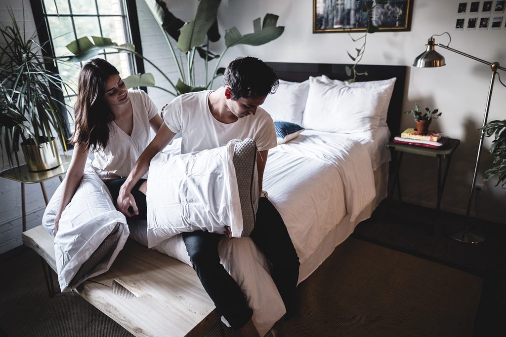 Couple sitting on edge of bed, man with head turned away from woman