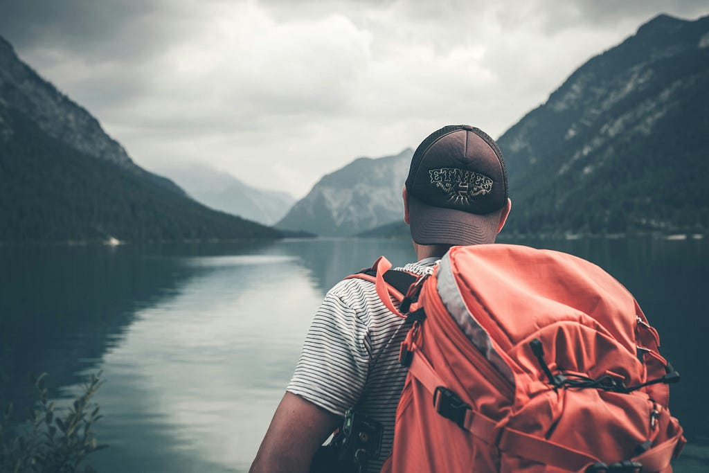 Backpacker traveling through mountain range and gazing out over an expansive body of water.