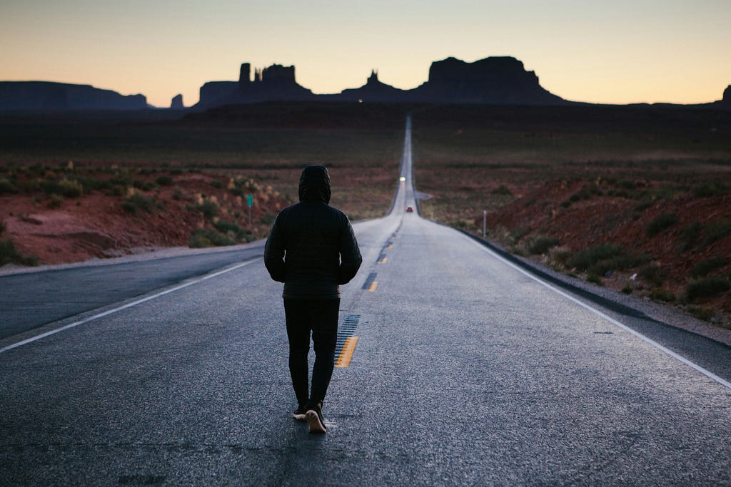 A person walking down a road at what seems like noon or night.