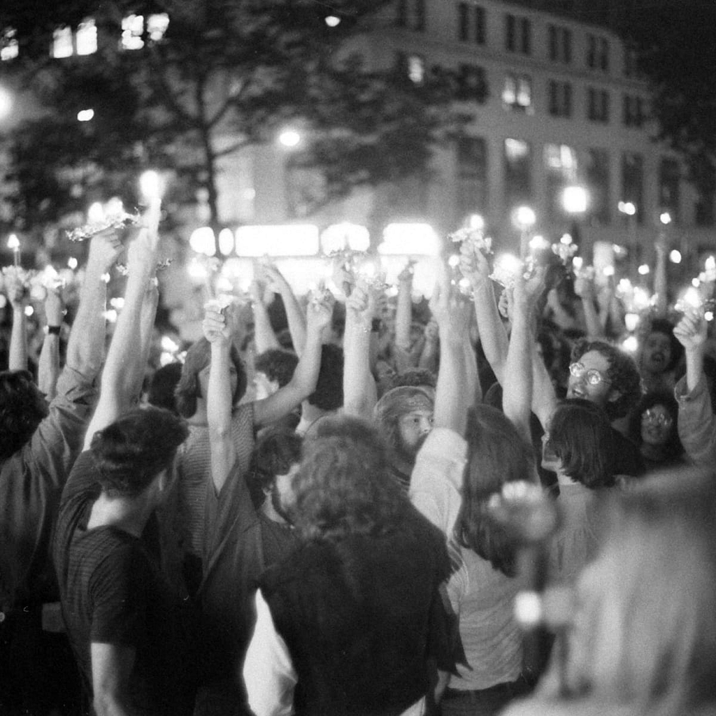 A black and white image showing people raising their hands in a protest. This picture represents the Stonewall Riot of 1969.