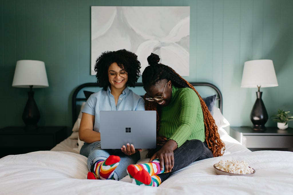 Two women on a bed smiling at a computer